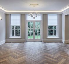 an empty room with two large windows and wood flooring in the center, along with chandelier