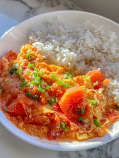 a white plate topped with rice and meat covered in tomato sauce on top of a table