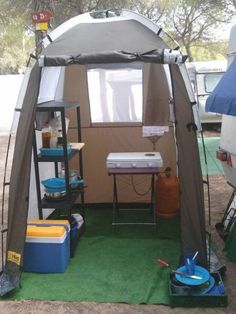 a tent with shelves and coolers in front of it on a green carpeted area