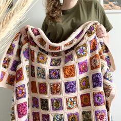 a woman holding up a crocheted blanket with flowers on the front and sides