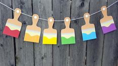 some paper cutouts are hanging from a string on a wooden fence with clothes pins attached to them