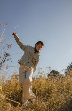 a man standing on top of a dry grass covered hillside next to tall grasses and trees