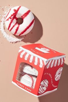 a box of candy cane next to a donut on a pink background with sprinkles