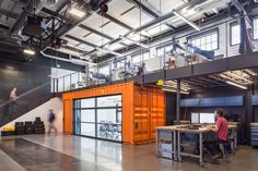 a man sitting at a desk in front of a large orange shipping container with stairs leading up to the second floor