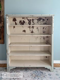 an old white painted bookcase with peeling paint on the front and bottom shelves, against a blue wall