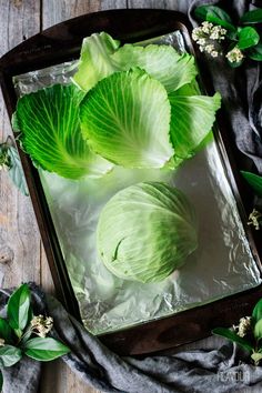 three heads of cabbage sitting on top of ice in a glass dish next to green leaves