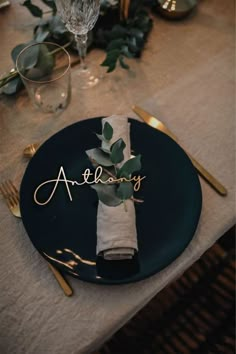 a black plate topped with a napkin and greenery next to a silverware holder