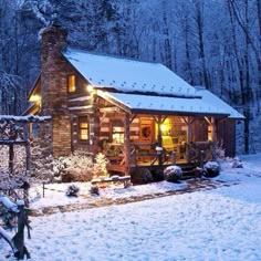 a cabin in the woods is lit up at night with lights on and snow covered ground