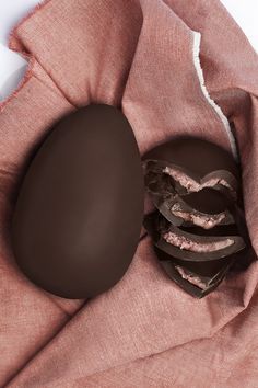 a heart shaped chocolate on top of a pink cloth next to some pieces of chocolate