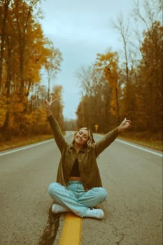 a woman sitting on the side of a road with her arms in the air