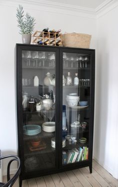 a black cabinet with glass doors and dishes on the top shelf in a white room