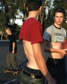 two young men standing next to each other in a parking lot with one man on a skateboard