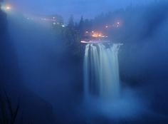 a large waterfall in the middle of a lake at night with lights shining on it