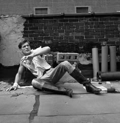 a man sitting on the ground with his arms behind his head, leaning against a brick wall