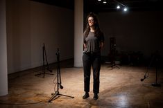 a woman standing in an empty room with microphones and lights behind her on the floor