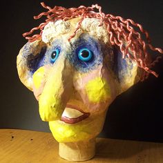 a clay head with blue eyes and braids on it's head sitting on a wooden table