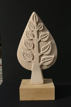 a carved wooden sculpture of a tree on a wood block with a black background in the foreground