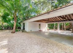 a white house surrounded by palm trees and gravel in front of it is a covered patio area