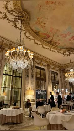 people are sitting at tables in a fancy restaurant with chandeliers hanging from the ceiling