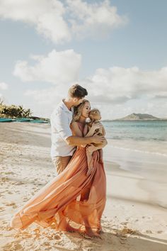 a man and woman hug on the beach as they stand in front of the ocean