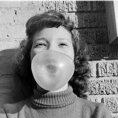 a woman blowing bubbles into her mouth in front of a brick wall