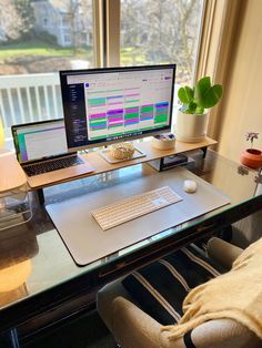 a glass desk with a laptop, monitor and keyboard on it in front of a window