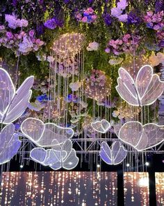 some lights that are hanging from the ceiling in front of flowers and plants on display