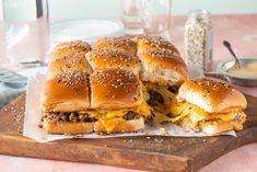 two cheeseburger sandwiches cut in half on top of a cutting board with other food items