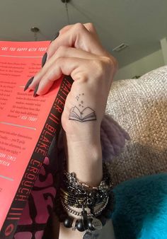 a woman's arm with a book tattoo on her left hand and a red book in the background