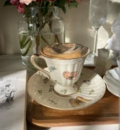 a tea cup and saucer on a wooden tray with flowers in vases behind it