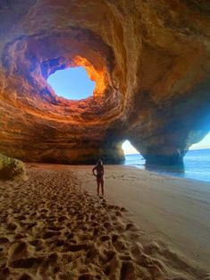 a man standing on top of a sandy beach under a cave