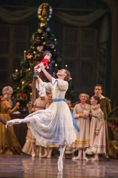 a ballerina is performing on stage in front of a christmas tree and other people