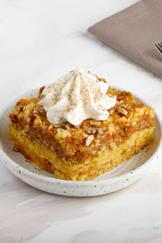 a white plate topped with a piece of cake covered in whipped cream