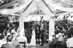 a bride and groom standing under a gazebo at their outdoor wedding ceremony in black and white