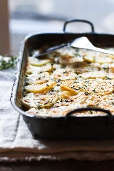 a casserole dish with cheese and vegetables in it sitting on a table next to a window