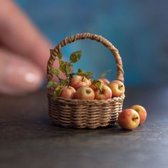 a basket filled with apples sitting on top of a table next to a person's hand