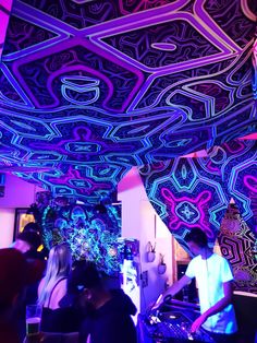 a group of people standing around in a room with neon lights on the ceiling and walls