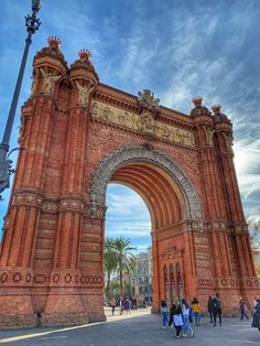 people walking in front of an old brick arch