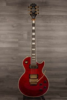 a red electric guitar sitting on top of a wooden floor next to a gray wall