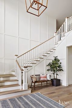 a white staircase with wooden handrails leading up to the second floor and a potted plant on the far side