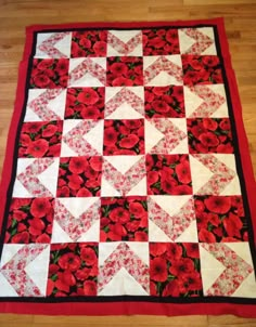 a red and white quilted table runner with flowers on the top, sitting on a wooden floor