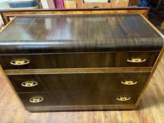 an antique chest of drawers with brass handles on a wooden floor in a room full of other furniture