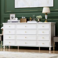 a white dresser sitting in a living room next to a lamp and painting on the wall