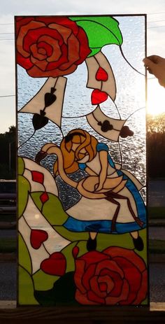 a stained glass window with flowers and people on the beach in front of water at sunset