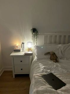 a laptop computer sitting on top of a bed next to a night stand and lamp