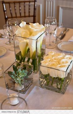 two vases filled with flowers on top of a table next to wine glasses and silverware