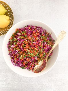 a white bowl filled with red cabbage and sprouts next to a gold spoon