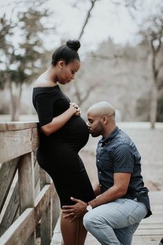 a pregnant woman leaning against a man on a bridge