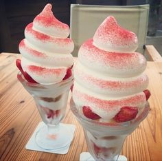 two ice cream sundaes with strawberries in them on a wooden table top