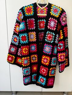 a colorful crocheted sweater hanging on a hook in front of a white wall